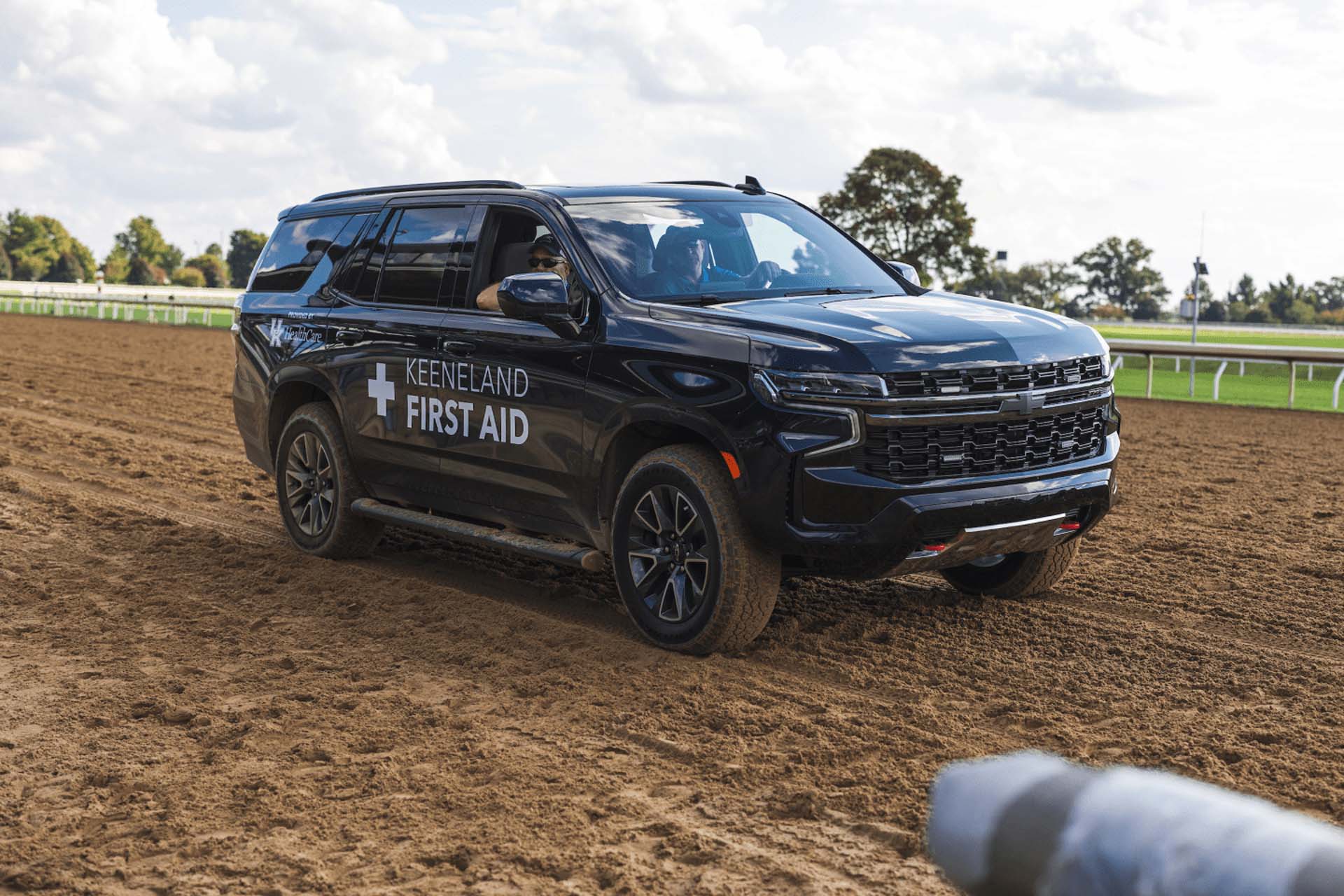 A picture of the Keenjockey First Aid car on the dirt track. It is a large black Chevy SUV.